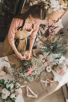 woman florist in beige apron is working in  flower shop. Floral design studio, making decorations and arrangements. Flower delivery, order creation. Small business. top view