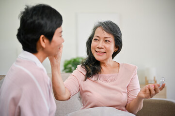 A happy middle-aged Asian woman applying makeup to her friend, helping her friend do makeup