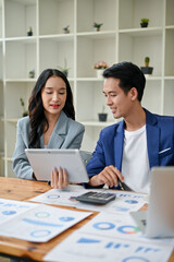 A businesswoman and a businessman are looking down at a tablet screen, discussing ideas