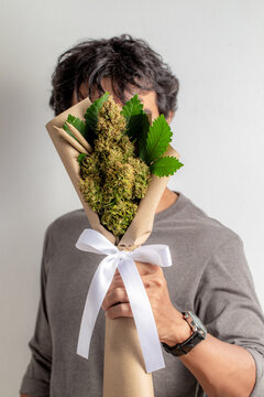 A man hand you a bouquet of marijuana tied with a white ribbon decorated with marijuana rolls