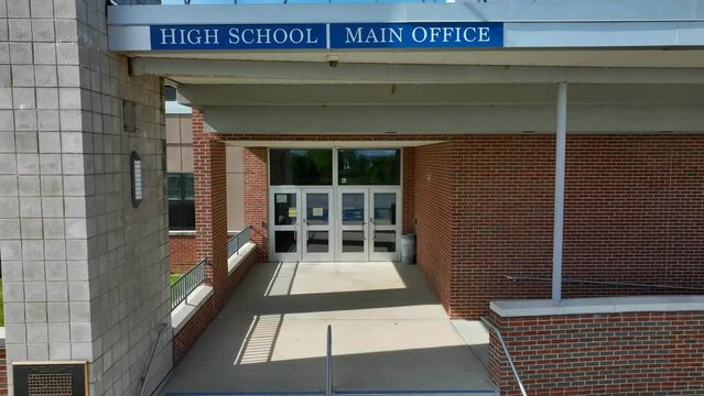 Aerial push in of main office entrance at American in school. High School, Main Office, visitors sign.