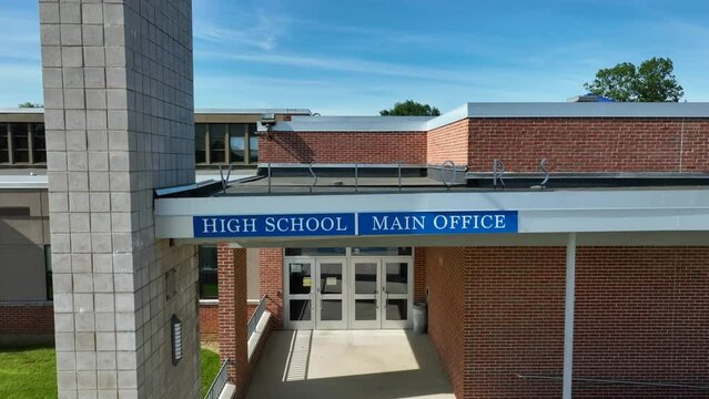 Visitor entrance of high school in America. USA schooling theme with American flag. Aerial rising shot.
