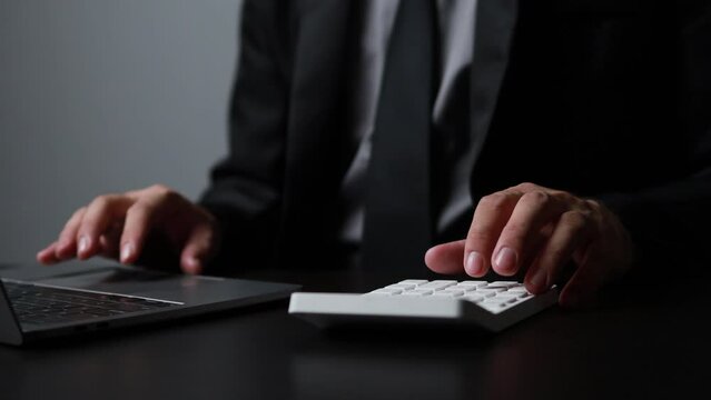 Businessman using a calculator to calculate numbers on a company's financial documents, he is analyzing historical financial data to plan how to grow the company. Financial concept.