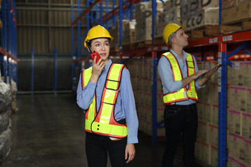 Group of warehouse workers with hardhats and reflective jackets using tablet, walkie talkie radio and cardboard while controlling stock and inventory in retail warehouse logistics, distribution center