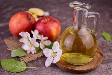 Glass decanter with apple cider vinegar and fresh apples on gray background.	