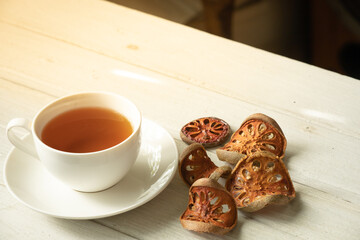 Cup of herbal tea and dried bael fruit on white wooden plate.