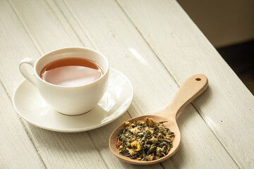 Cup of herbal tea and dried flower tea on white wooden plate.