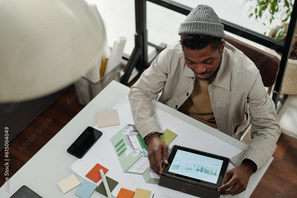 Aufkleber Above view of young African American specialist using tablet with graphic sketches on screen while sitting by desk and working over new project