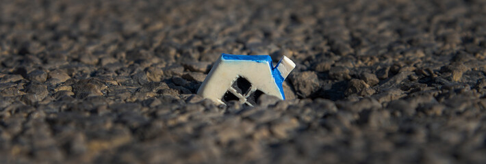 Miniature white toy house fallen into a crack in the earth.Closeup.Banner advertisement.