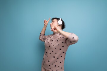 active bright caucasian young woman with a short haircut dressed in a beige suit listens to music in wireless bluetooth headphones