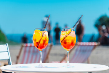 Glasses of orange spritz aperol drink cocktail on table outdoors with sea and trees view blurred...