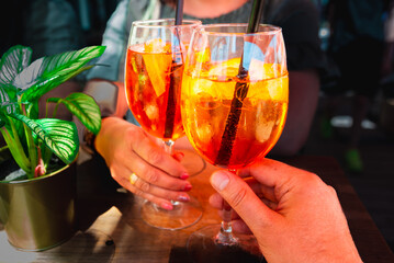Couple celebratory toast with aperol spritz orange alcoholic cocktails at outdoors cocktail bar at...