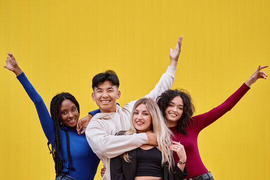 Happy multi-ethnic friends posing together in front of a yellow wall. Friendship concept.