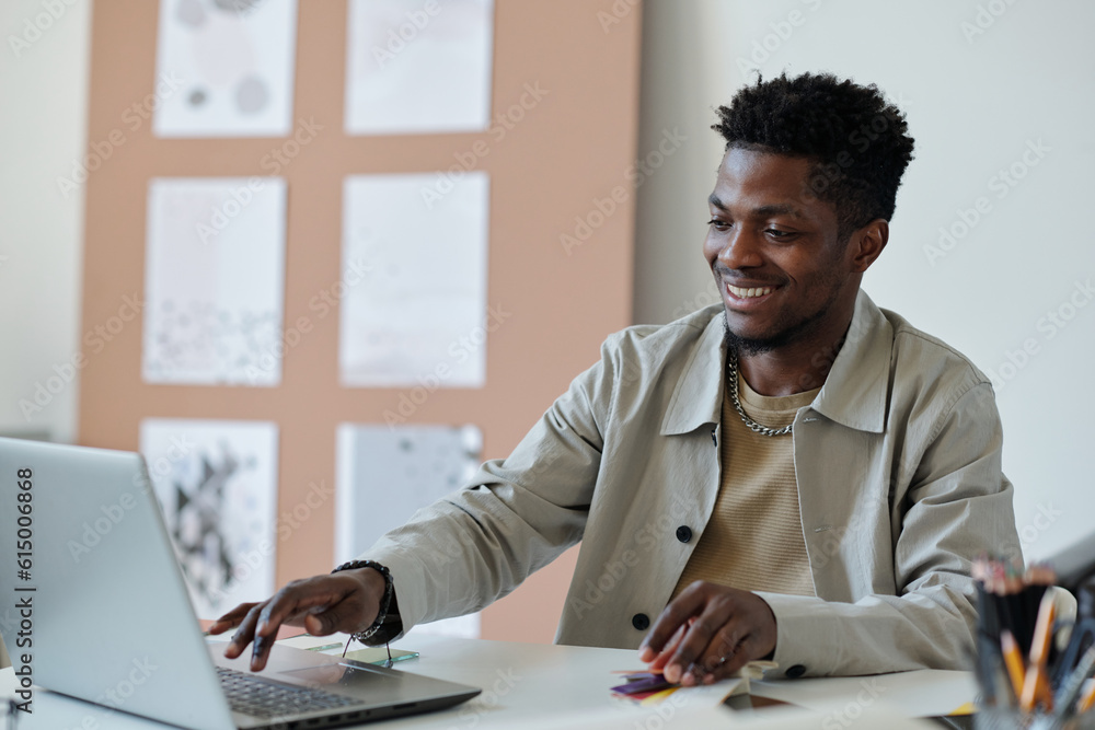 Aufkleber young smiling african american male webdesigner pressing key of laptop keyboard while sitting by wor