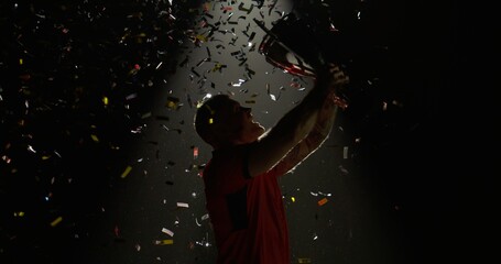 Silhouette of Caucasian male rugby player raising a trophy above head against bright light and...