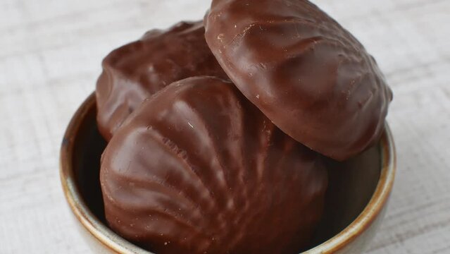 Chocolate zephyr slices stacked in a beige cup. Marshmallows in chocolate glaze folded in a brown bowl on a light table close-up. Sweet happiness. Chocolate delight and pleasure