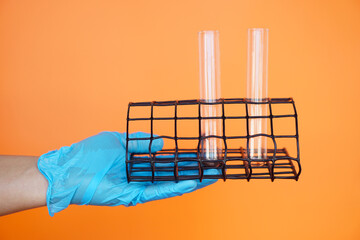Close up hand wears blue glove, holds test tubes on rack for tube holder, isolated on orange...