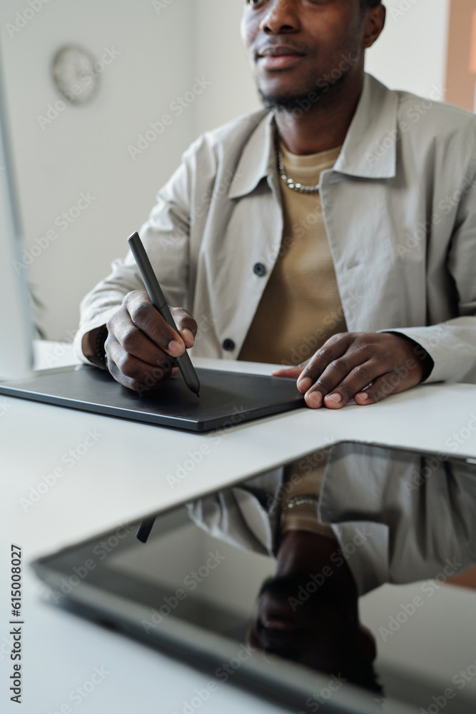 Poster close-up of young black man sitting by workplace in front of computer screen in office and drawing g