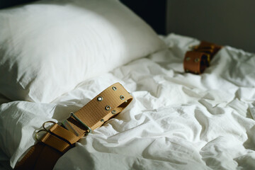 Close-up of bed with white pillow and several tight brown belts prepared for patient of lunatic...