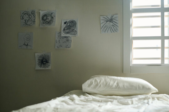 Interior of ward of mental hospital with group of pictures drawn by patients of lunatic asylum on wall and bed with sheet and pillow