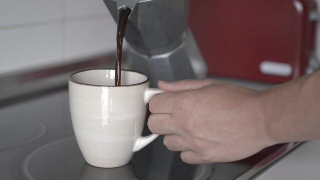 Anonymous person pouring coffee from his Italian coffee maker into his cup. Unrecognizable man's hands preparing a fresh coffee in his kitchen.