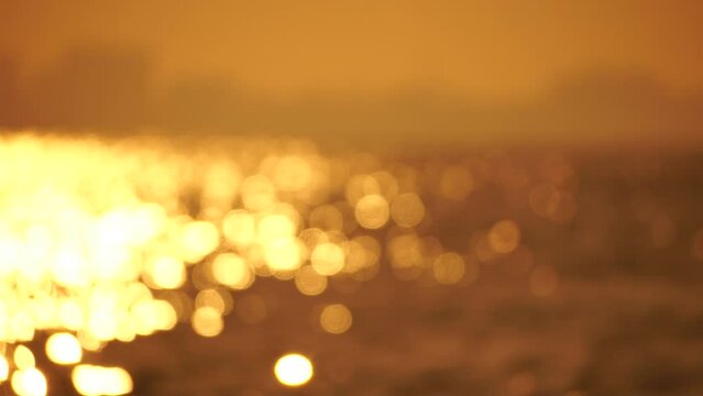 Blurred golden sea at sunset. The sun reflects and sparkles on the waves with bokeh, illuminating the golden sea. Holiday recreation concept. Abstract nautical summer ocean sunset nature background.