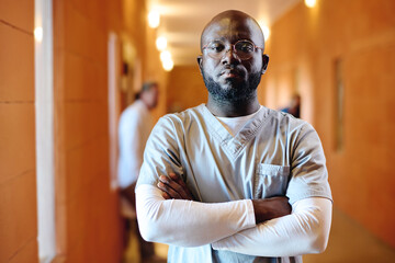 Young serious African American male assistant in uniform and eyeglasses keeping his arms crossed by chest and looking at camera in clinics