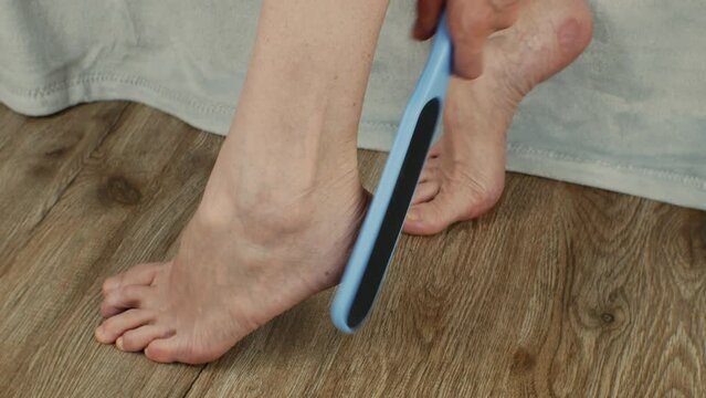 The female uses a sanding brush to exfoliate her foot. Treatment of cracked heels in women. A woman makes cosmetic procedures with a plastic grater for the skin of the heels. Callus removal concept
