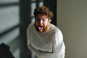 Young insane man in straitjacket showing tongue and screaming while standing in front of camera in...