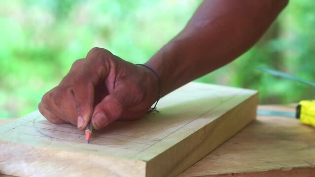 indian artisan drawing a circle with a pencil on a wood before starting the cutting process 