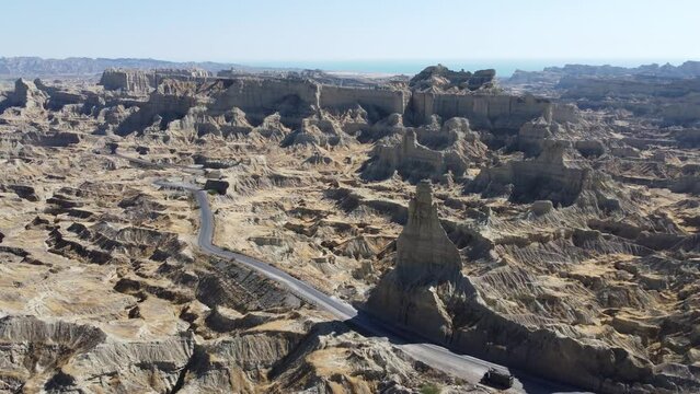 Aerial drone forward moving shot over winding road alongside Buzi Top in Makran, Balochistan, Pakistan on a bright sunny day.