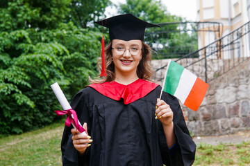 Young italian woman wearing graduation gown and hat holding flag of Italy smiling happy and...