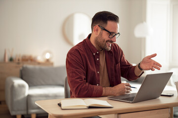 Obraz premium Smiling man having an online meeting with his colleagues, talking about the work.