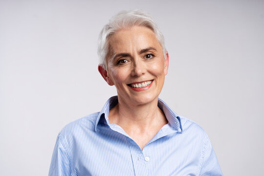 Portrait of smiling senior woman, wearing stylish, casual shirt, looking at camera isolated on gray background. Confident middle aged female posing for picture in studio