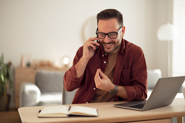 Smiling man making a phone call, taking a break from work, laughing and talking to one of his friends.