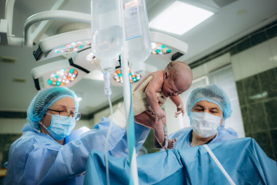 The medical team performing cesarean sections. The doctor hold the baby giving birth to his mother to see.
