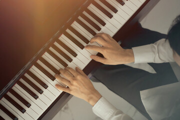 male musician hands playing on piano keys, black and white with golden light overlay.