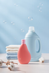 Blue and pink plastic bottle of laundry detergent with cotton towels and branch of cotton in the background. Delicate wash concept - obrazy, fototapety, plakaty