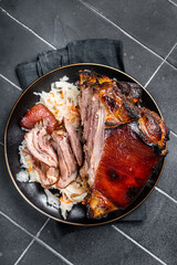 Roast Pork Ham Hock, knuckle with Sauerkraut on a plate. Black background. Top view