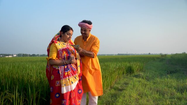  A hardworking and proud Indian farmer and his wife stand together in their field, surrounded by nature's bounty. They rejoice in a bountiful harvest that brings them good cash returns.
