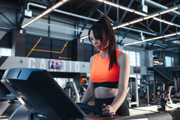 Fototapeta na wymiar Adult sporty woman workout on treadmill in modern fitness gym. Lady brunette running in interior sports center, exercises treadmill. Cardio working out and sport training concept. Copy ad text space