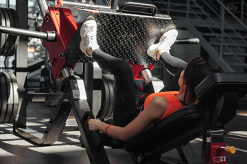 Sporty lady workout legs extension push machine in fitness gym. Woman in sportswear exercising legs...
