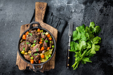 Beef stew with potato, carrot and herbs in a skillet. Black background. Top view