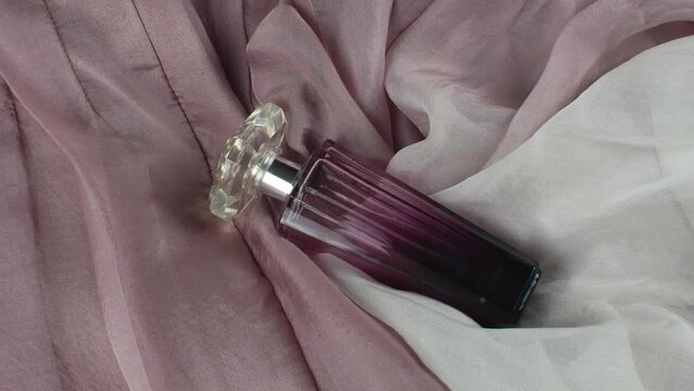 A female perfume in an original transparent glass bottle, on a pink silk folded background of fabric in different shades. Flat lay. View from above