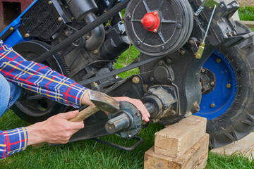 replacement of tractor wheels,a man works with a hammer, knocking out a wedge on a tractor shaft