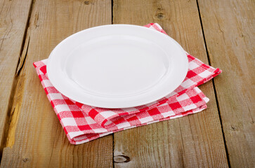 Empty plate on red-white checkered tablecloth in an old wooden table
