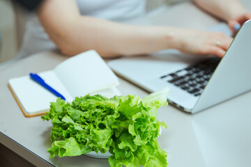Snack during working hours. A woman at remote work at home eats vegetables and lettuce, diet food as a part of healthy lifestyle.
