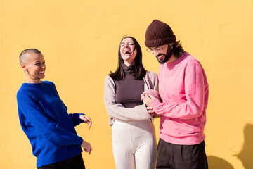 joyful young people laughing and having fun together on yellow background, concept of friendship...