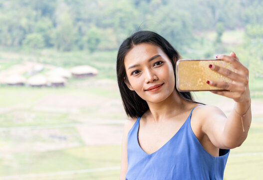 A young woman with a smartphone takes a selfie photo in a tropical landscape