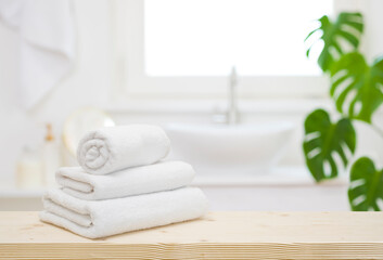 Fototapeta na wymiar White folded towels on wooden table top in blurred bathroom